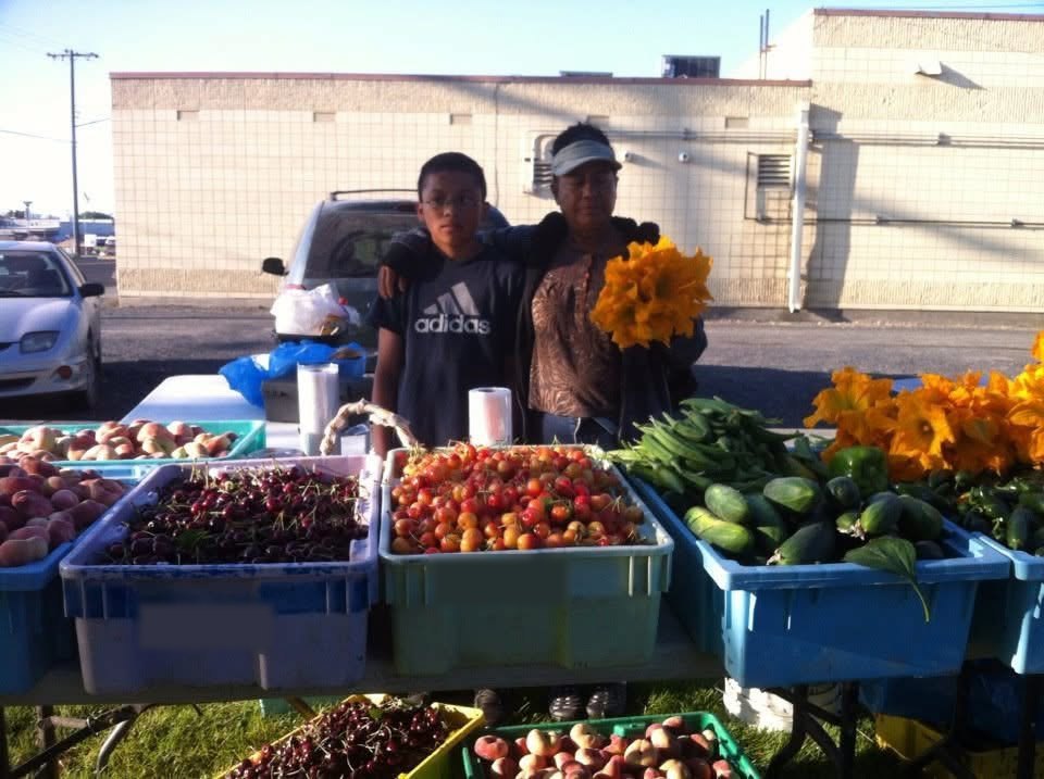 Isaias de niño junto a su abuela en el puesto de fruta de la familia, con cajas de cerezas y duraznos al frente.